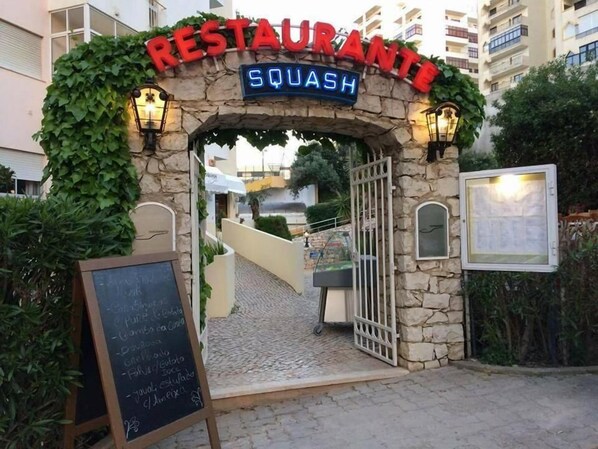 L'ingresso di un ristorante con un arco in pietra, un'insegna al neon e una lavagna con il menu.