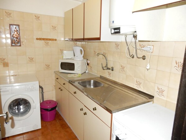 A compact kitchen with a washing machine, a sink, a microwave, and a small countertop. - Squash Club (Portimão)