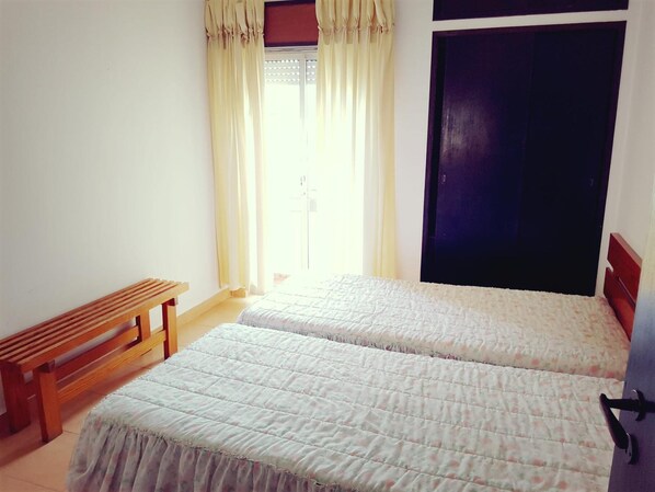 A bedroom with two beds, a wooden bench, and a dark door.