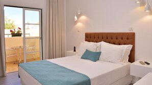 A hotel room with a bed, a nightstand, a bedside table, a lamp, a sliding glass door to a balcony, and a view of the outside.