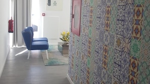 A hallway with patterned tiles, a blue chair, a door with a red handle, and a fire extinguisher on the wall.