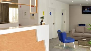 A modern reception area with a wooden reception desk, a blue chair, a sofa, and a television mounted on the wall.