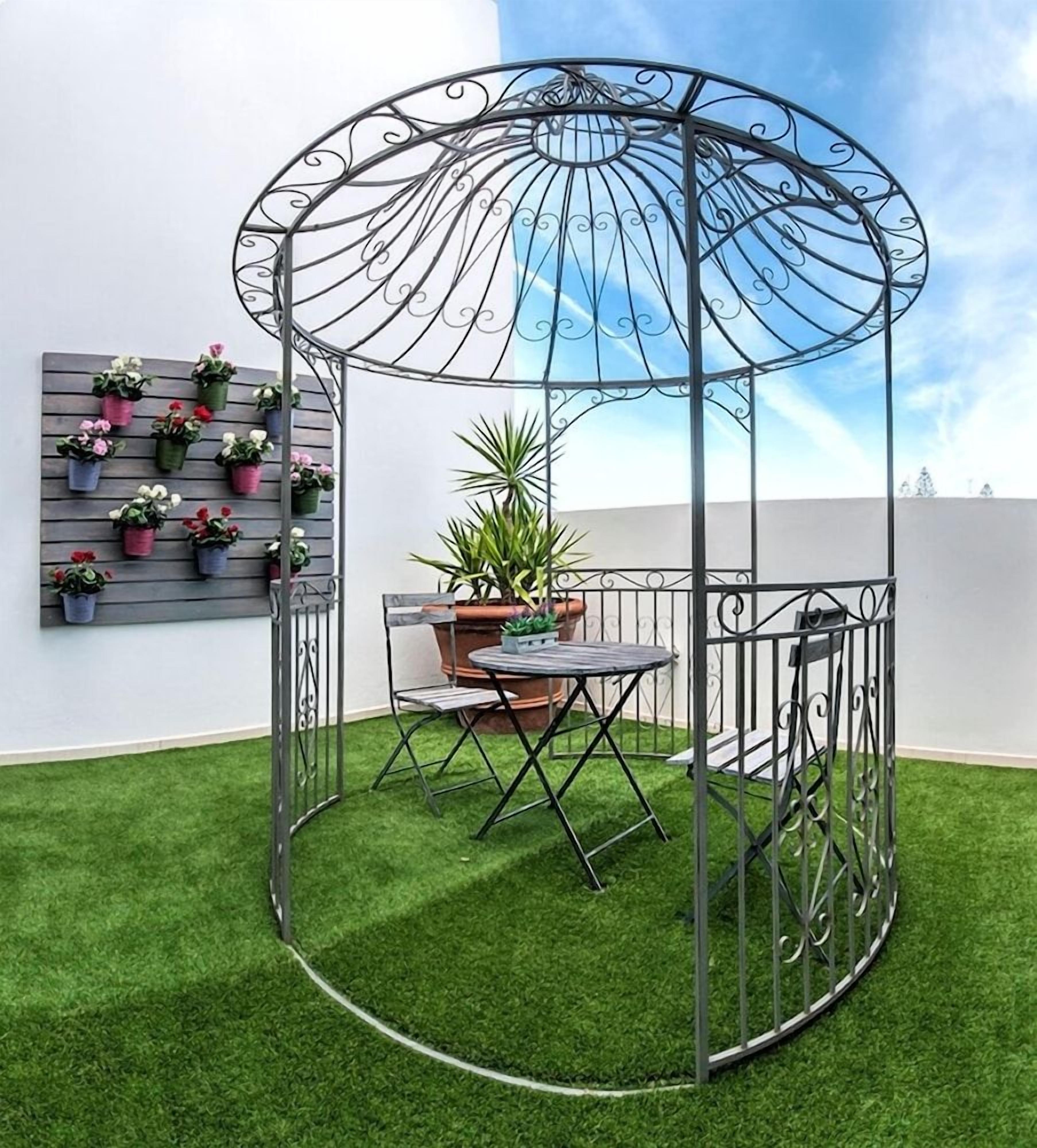 A metal gazebo with a glass roof, surrounded by artificial grass, and a potted plant in the center.