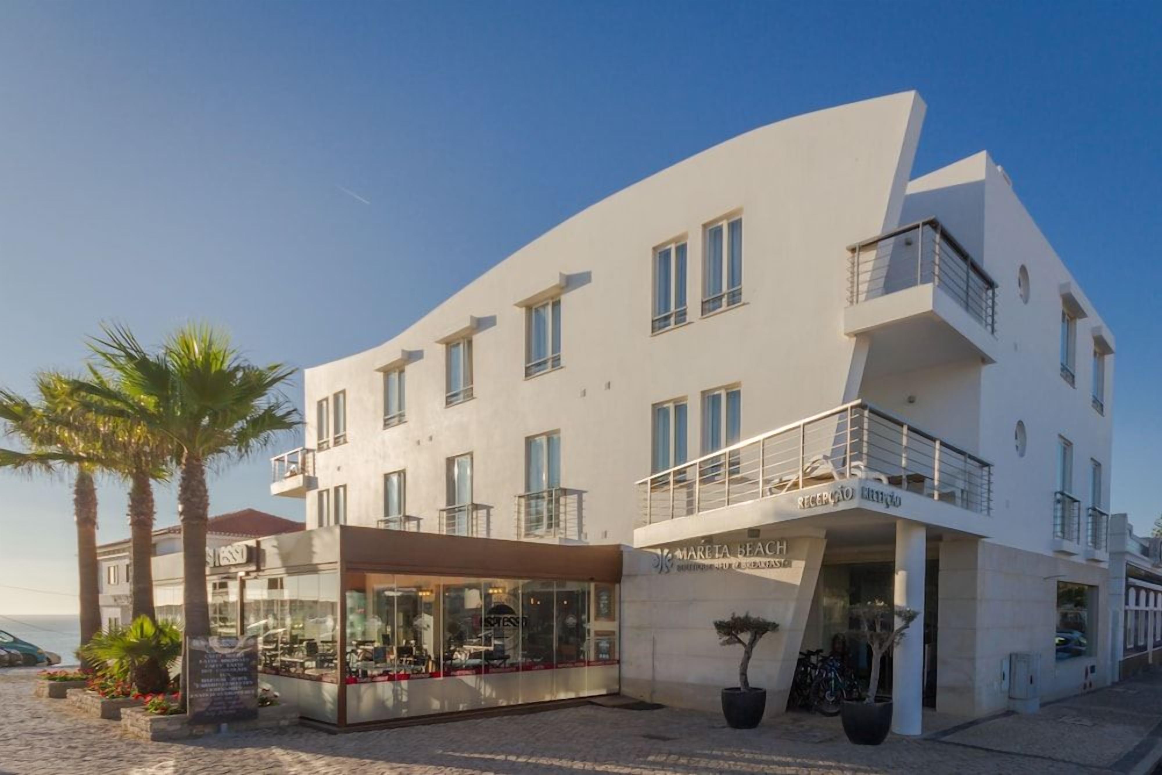 Un hotel moderno con fachada curva, varios balcones y un restaurante con terraza.