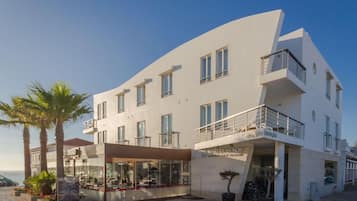 Un hotel moderno con fachada curva, varios balcones y un restaurante con terraza.