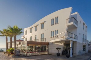 Un hôtel moderne à la façade incurvée, doté de nombreux balcons et d’un restaurant avec une terrasse.