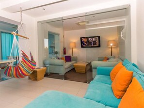 Una sala de estar moderna con un sofá azul turquesa, una hamaca colorida y un televisor de pantalla plana.