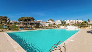 A swimming pool with clear blue water, surrounded by lounge chairs and umbrellas, with buildings in the background. - Senhora Da Rocha (Lagoa)