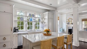 Una cocina amplia con armarios blancos, una isla grande con taburetes y vistas al exterior a través de amplios ventanales.