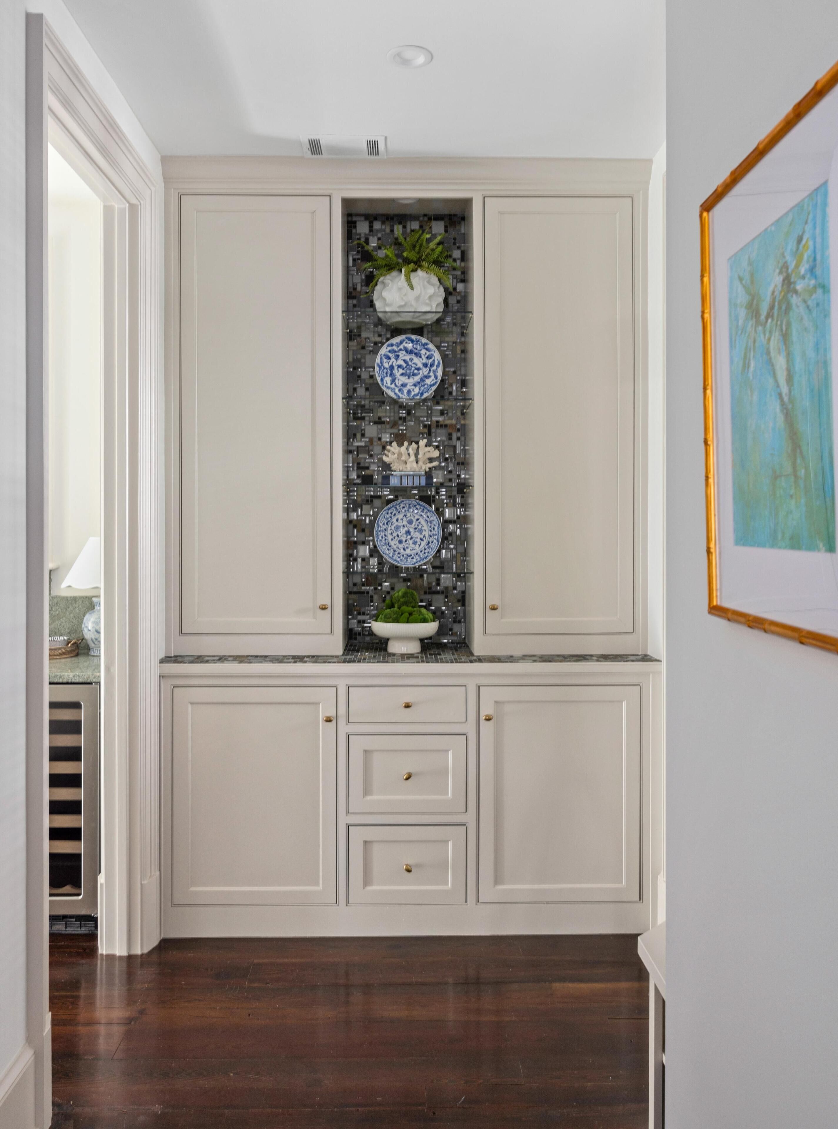 A kitchen with white cabinetry, a backsplash with mosaic tiles, and a wooden floor.