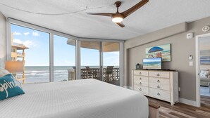 Un dormitorio con una cama grande, ventilador de techo, televisión y vista al océano.