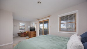 Un dormitorio con cama, cómoda, televisor y puerta corrediza de vidrio que da a un balcón.