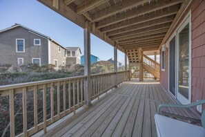A wooden deck with a railing, a staircase leading to a covered area, and a view of neighboring houses. - 6077- Sunshine Daydream - Nags Head Coastal Retreat Near Beach (Nags Head)