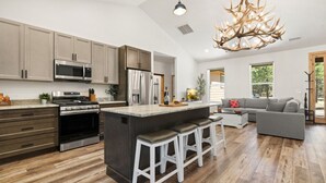A modern kitchen with a large island, stainless steel appliances, and a unique chandelier.