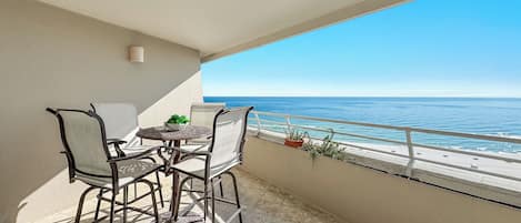 Uma varanda com mesa e cadeiras, um vaso de planta e vista para o mar.
