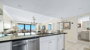 Une cuisine moderne dotée d’un grand îlot central, d’appareils électroménagers en acier inoxydable et offrant une vue sur l’extérieur.