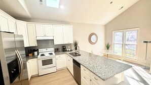 A modern kitchen with white cabinets, stainless steel appliances, granite countertops, and a large window providing natural light. - Large Cary Family Home-3 King Beds, Fenced Yard, 3 full bathrooms (Cary)