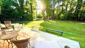 An outdoor patio area with wicker furniture, a bench, and a grassy lawn. - Large Cary Family Home-3 King Beds, Fenced Yard, 3 full bathrooms (Cary)