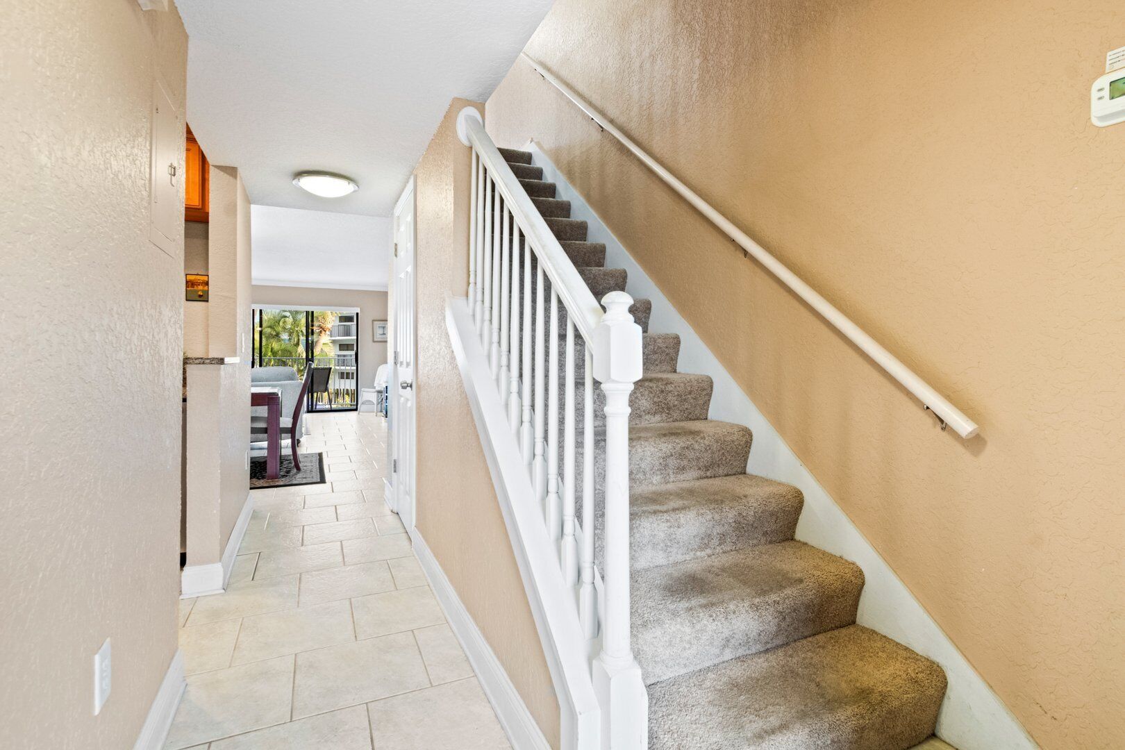 A staircase with beige walls and white railings leading to an open area with a view of the outdoors.