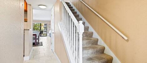 A staircase with beige walls and white railings leading to an open area with a view of the outdoors.