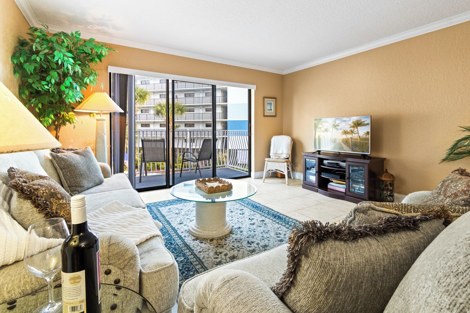 A living room with a sofa, a glass coffee table, a TV, and a balcony with a view of the sea.