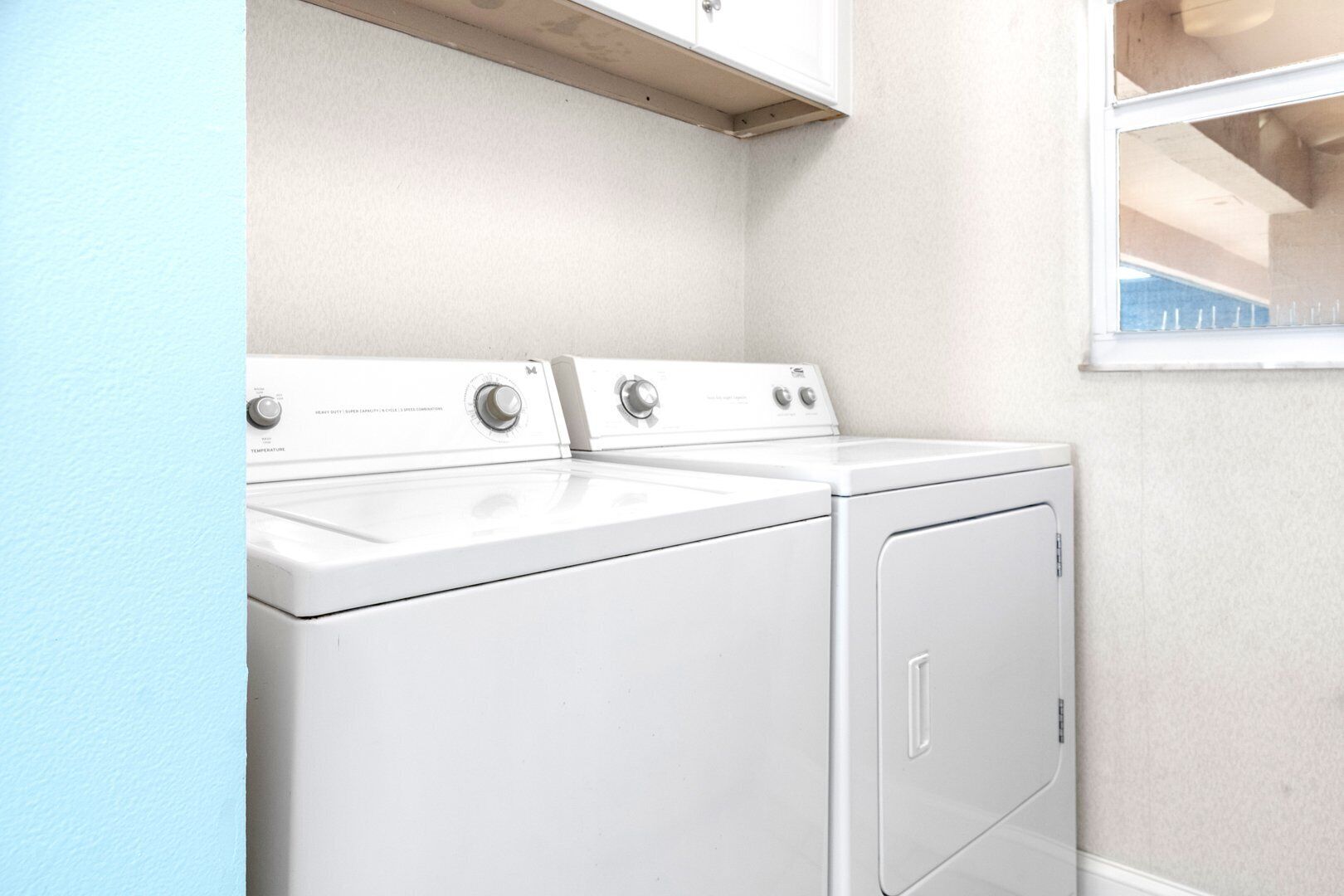A laundry area with a front-loading washer and dryer, a window, and a light blue wall.