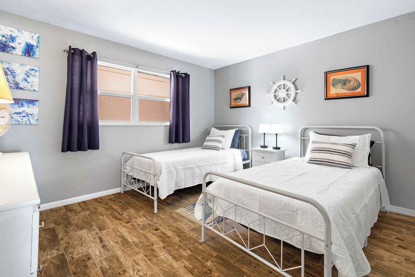 Un dormitorio con dos camas individuales, una ventana con cortinas, un reloj de pared y cuadros enmarcados.