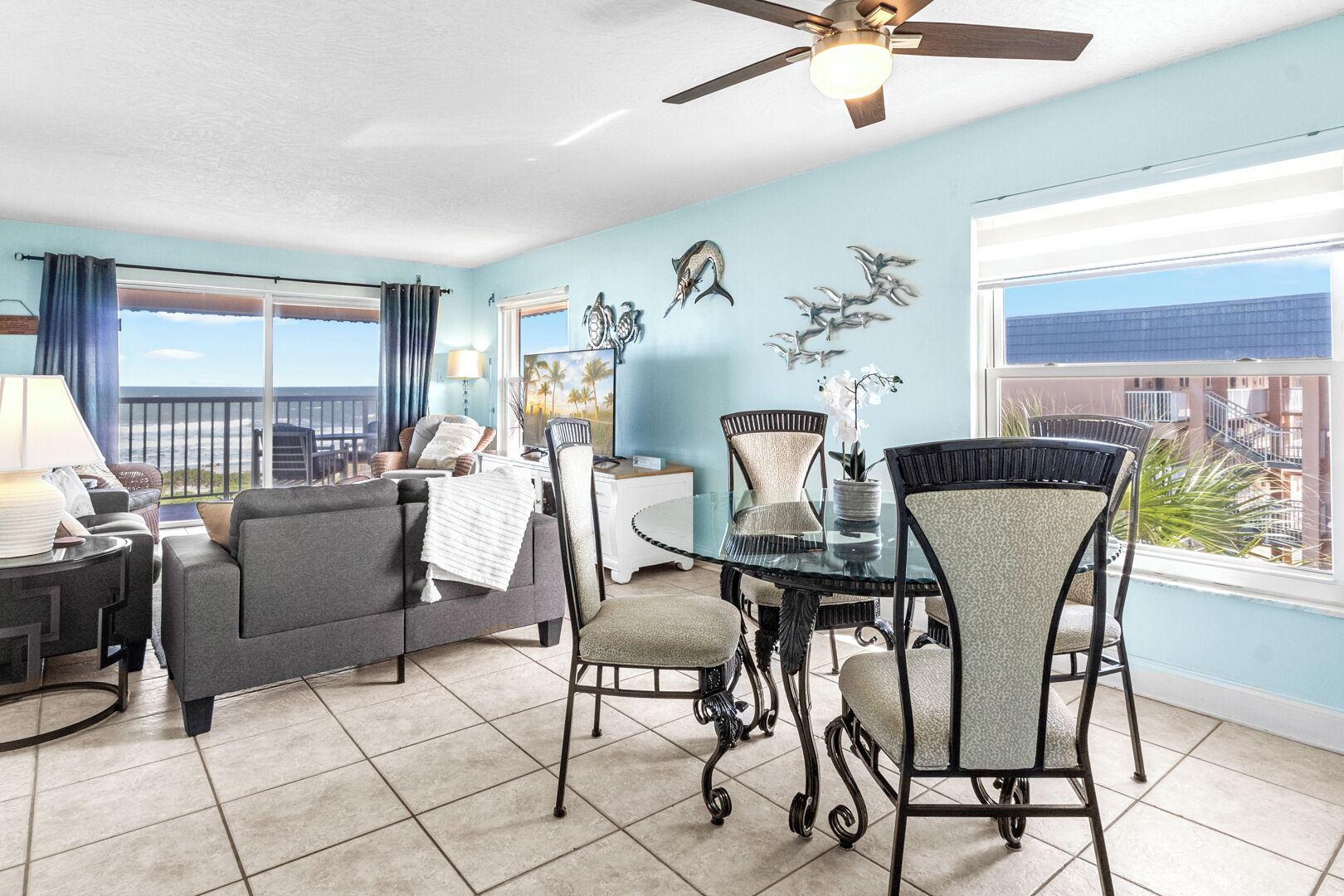 A spacious living room with a glass dining table, comfortable seating, and a view of the ocean.