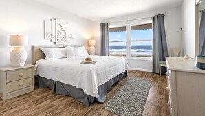 A bedroom with a large bed, two bedside tables, a desk, a chair, and a view of the ocean. - Gorgeous Direct Oceanfront w/ Private Balcony, Heated Pool & BBQ Grill! 🌊 (Cocoa Beach)