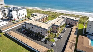 A multi-story hotel with a parking lot, adjacent to a beach and ocean. - Gorgeous Direct Oceanfront w/ Private Balcony, Heated Pool & BBQ Grill! 🌊 (Cocoa Beach)