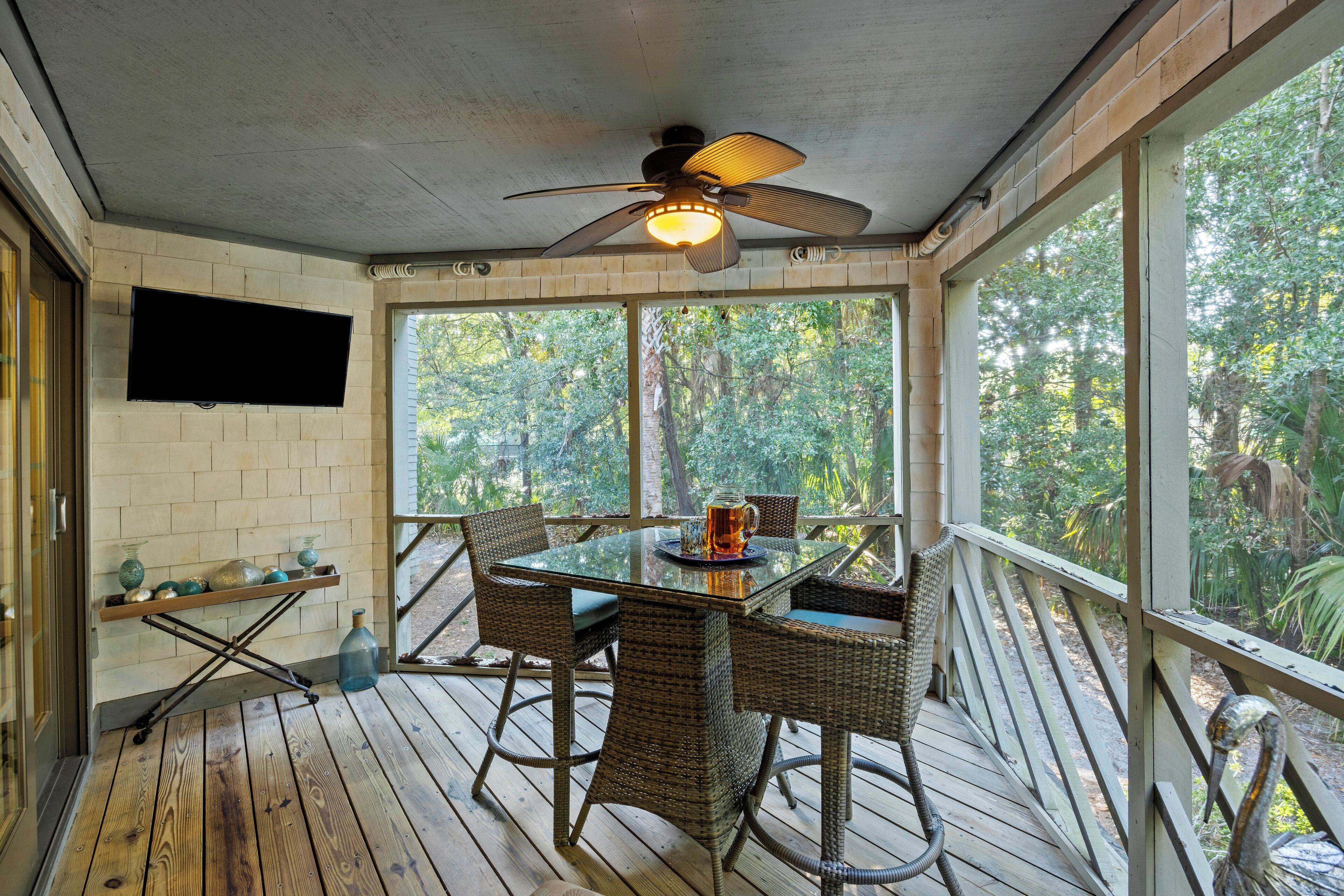 A covered outdoor area with a table and chairs, a ceiling fan, and a TV mounted on the wall.