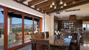 Une salle à manger spacieuse, dotée d’une grande table et de chaises, d’un lustre et offrant une vue sur le paysage urbain grâce à de grandes fenêtres.