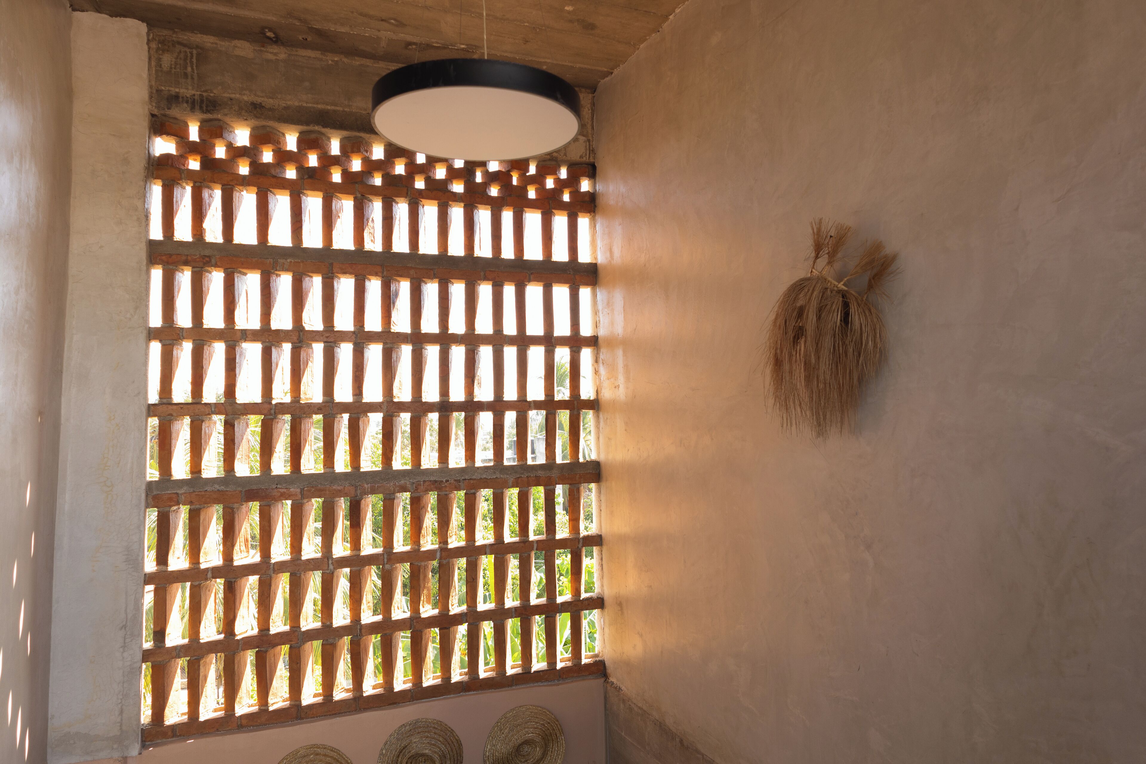 Una habitación con ventana de celosía de madera, lámpara colgante y cestas tejidas en la pared.
