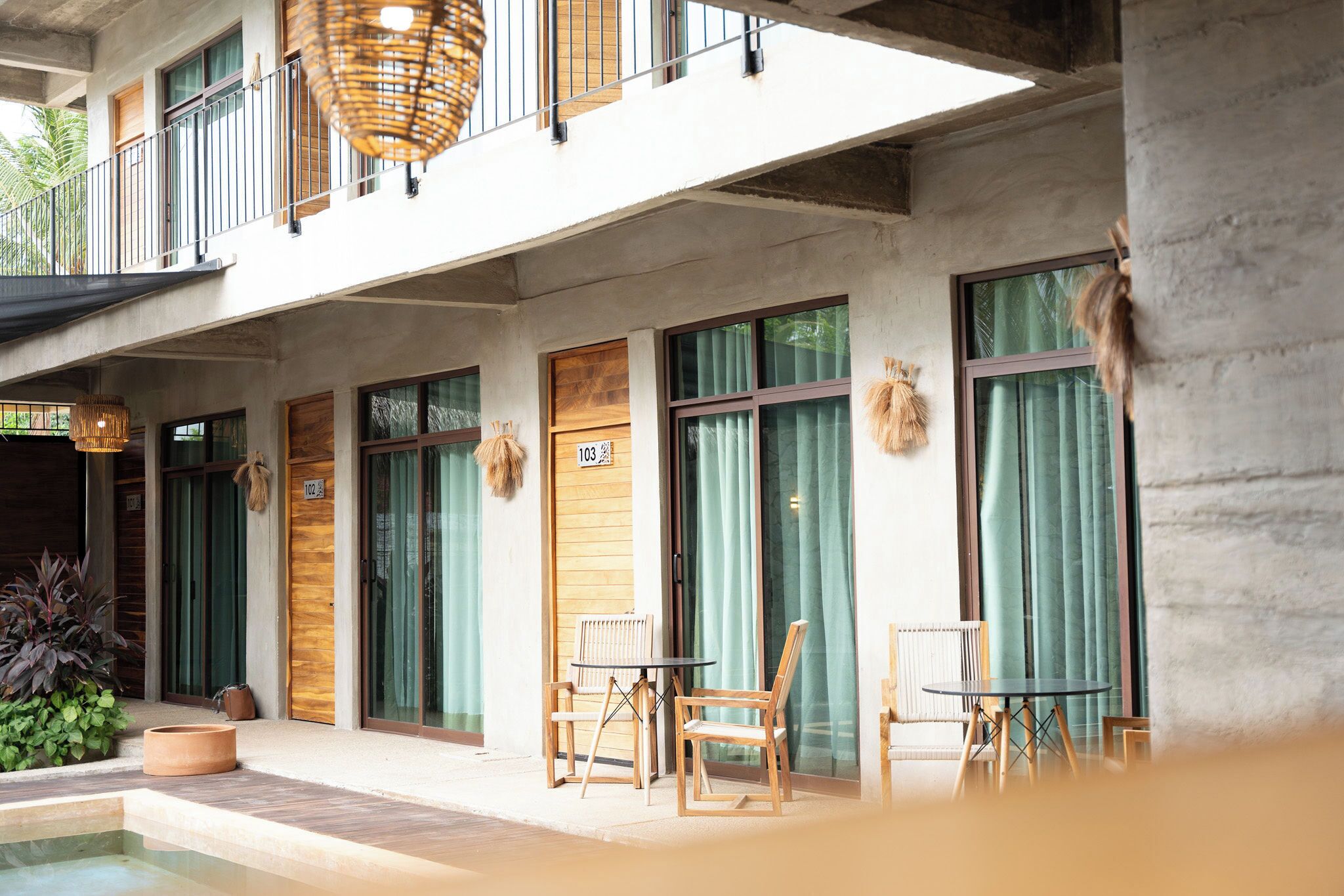A hotel with a pool, wooden doors, and a balcony with wicker furniture.