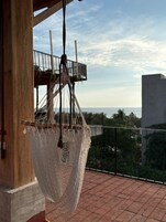 Una hamaca colgada en un balcón con vista al océano y un edificio al fondo.
