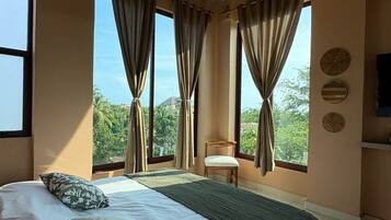 Ein Schlafzimmer mit einem großen Bett, einem Deckenventilator und mehreren Fenstern mit Vorhängen.