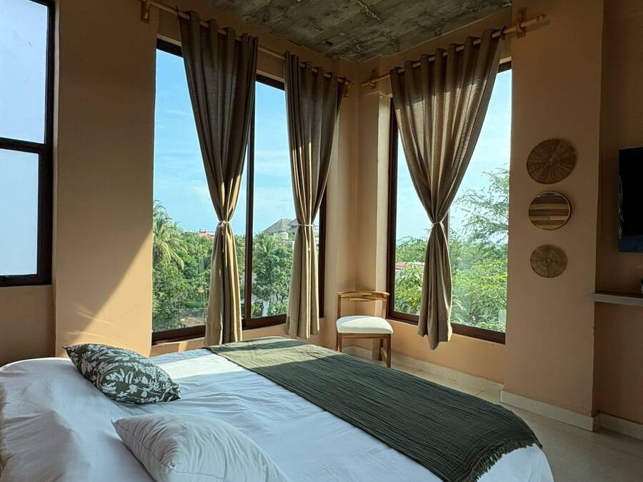 Ein Schlafzimmer mit einem großen Bett, einem Deckenventilator und mehreren Fenstern mit Vorhängen.