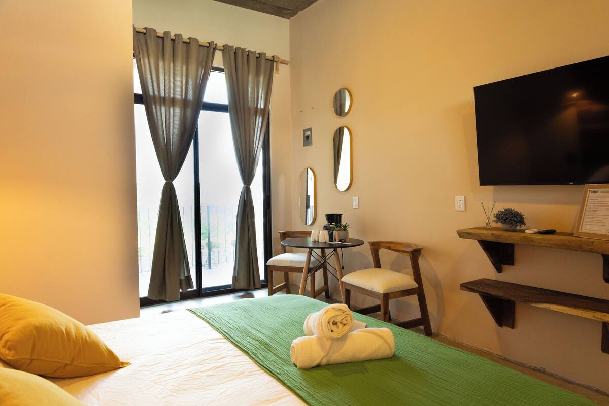 Une chambre d’hôtel avec un lit, une couverture verte, une serviette, une télévision, un bureau et une chaise.