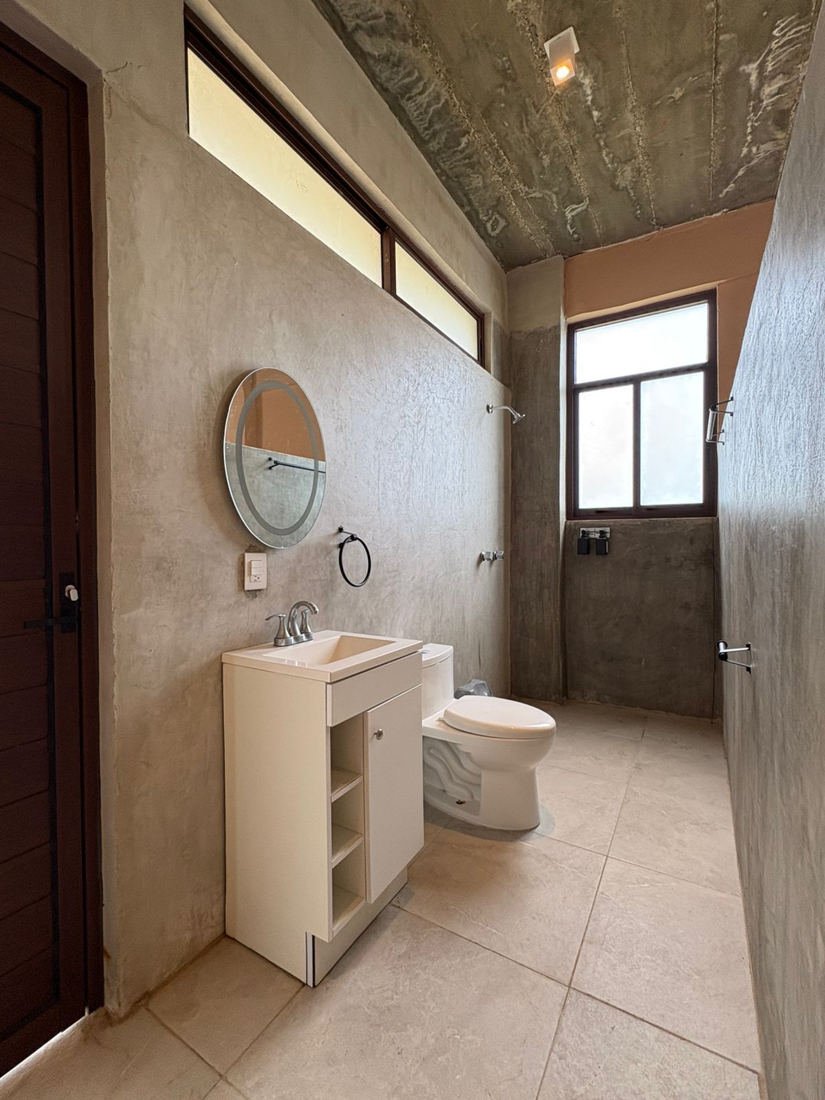 A bathroom with a toilet, sink, and mirror. There is a window providing natural light.