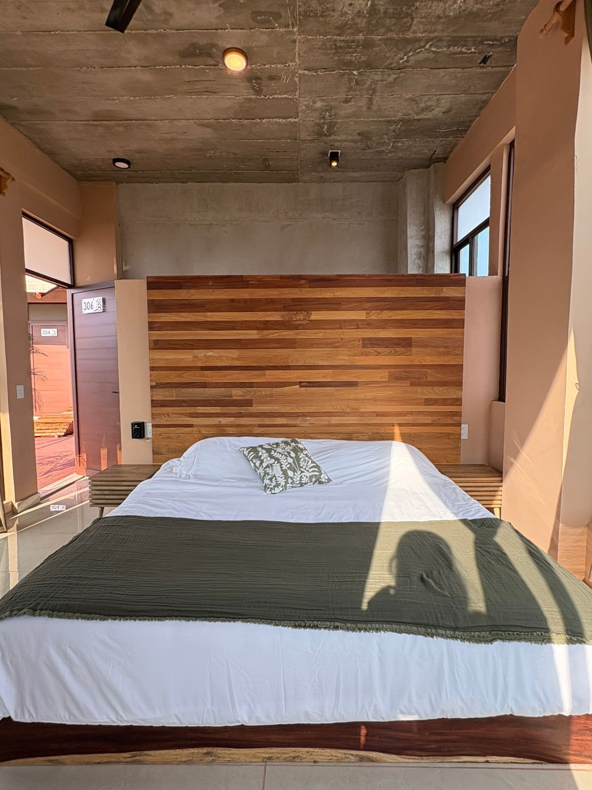 A modern bedroom with a wooden headboard, a large bed with white bedding, and a view of the outside through a window.
