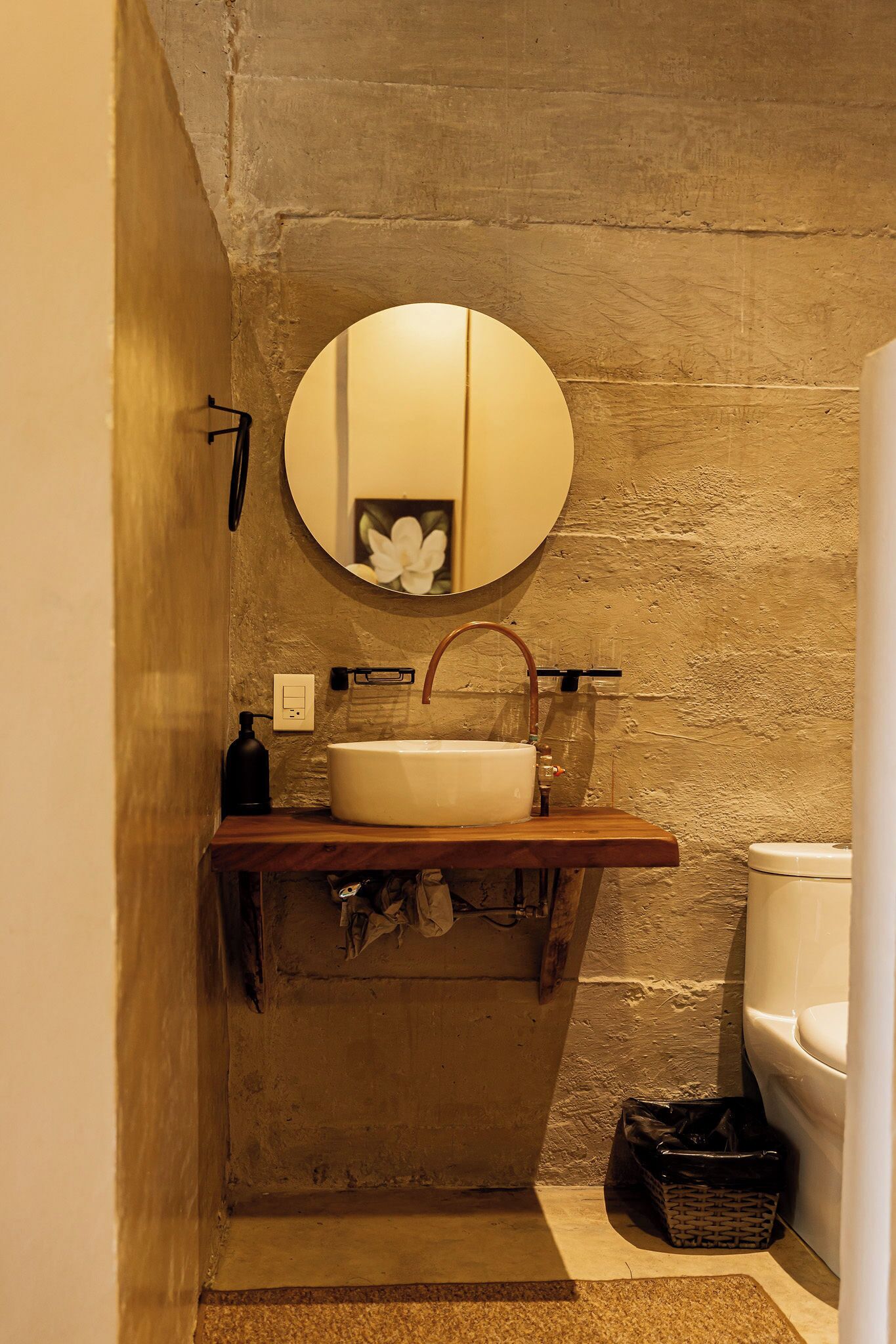Une salle de bain avec un miroir rond, un lavabo blanc et un plan de toilette en bois.