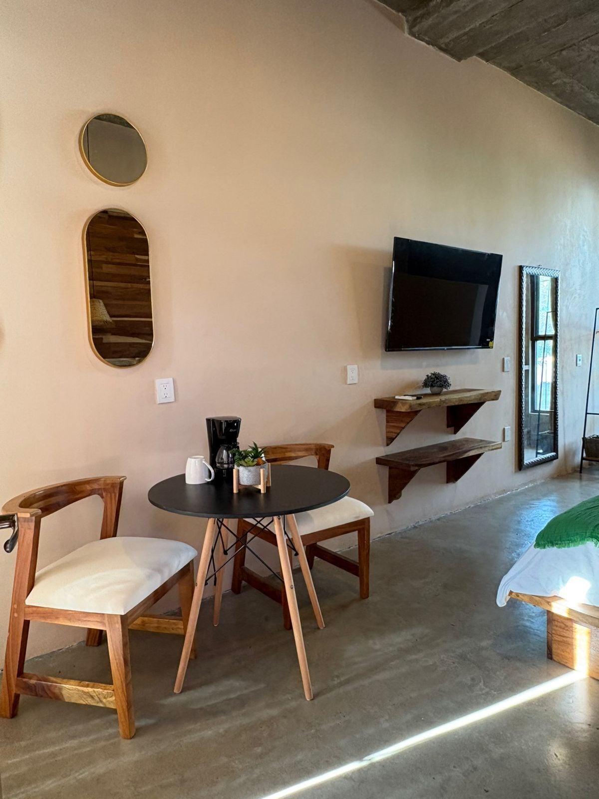 A cozy room with a round table, two wooden chairs, a coffee maker, and a TV mounted on the wall.