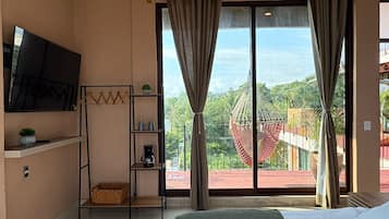 A hotel room with a bed, a TV, a shelf with items, and a view of the outdoors.