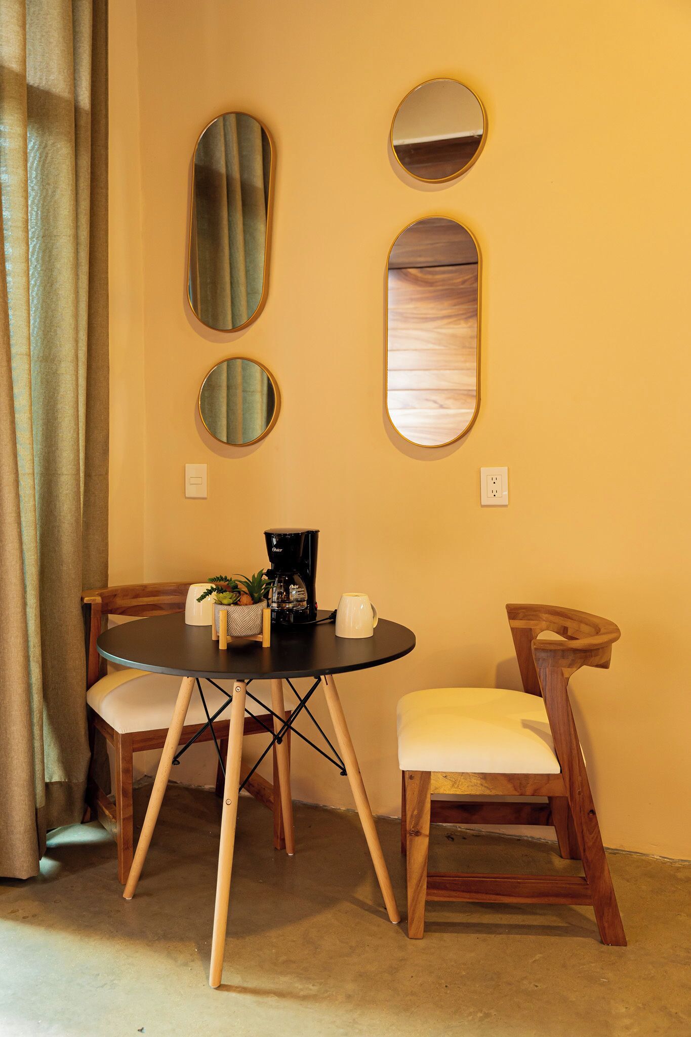 A room with a round table, two chairs, and three wall-mounted mirrors.