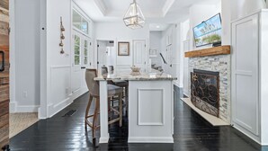 A spacious kitchen with a central island, a fireplace, and a television mounted above it. - Tannin Luxe 3BR + Loft Bunks, Steps To Beach Access, Pool, Firepit, Water Views (Orange Beach)