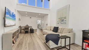 A spacious living area with a high ceiling, a dining table, a sofa, and a bookshelf. - Venice Beach Two Bedroom Private Condo with Community Pool, Gulf Beach Access and Water Views! (Venice)