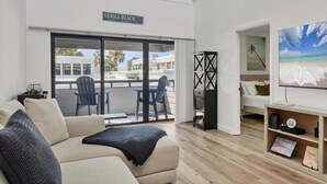 A living room with a large window, a sofa, a coffee table, and a bookshelf. - Venice Beach Two Bedroom Private Condo with Community Pool, Gulf Beach Access and Water Views! (Venice)