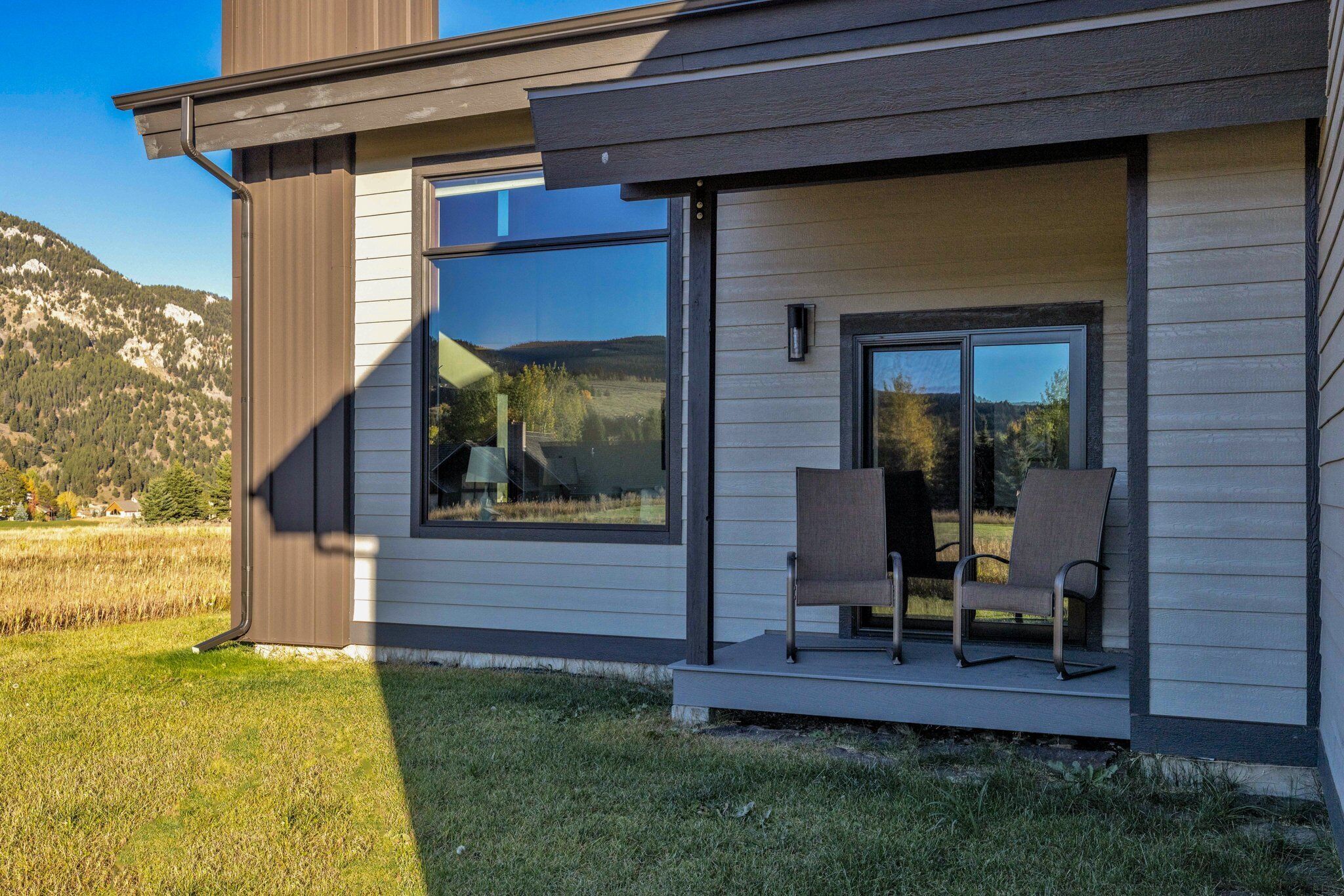 Een modern huis met een groot raam en een veranda met twee stoelen.