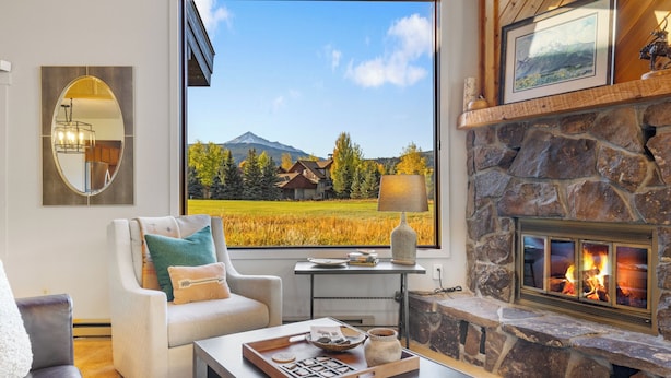 Una sala de estar acogedora con chimenea, un ventanal con vistas a la montaña y un espacio de estar confortable.