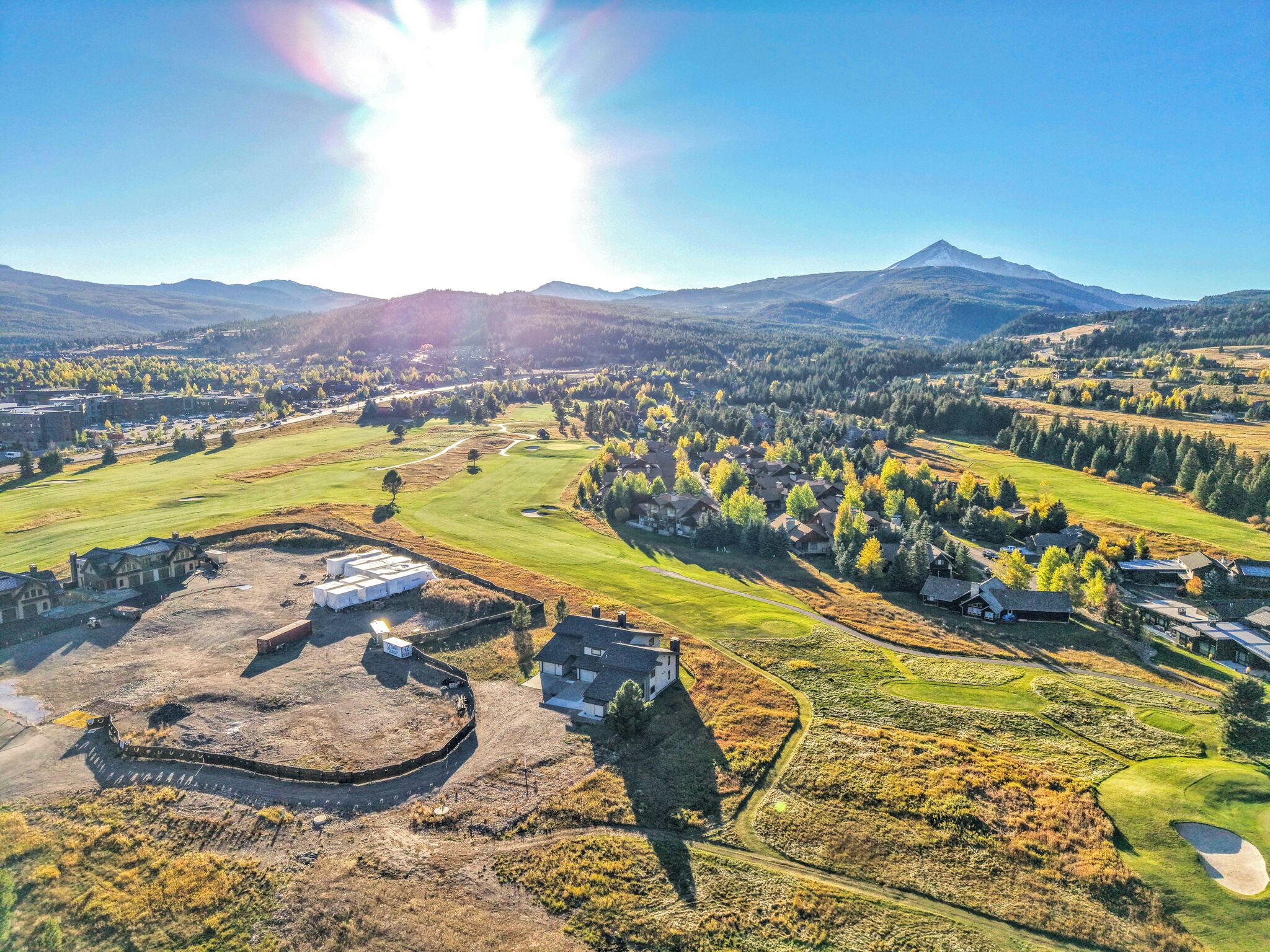 Vista aérea de un campo de golf con edificios residenciales, un extenso campo abierto y una montaña al fondo.